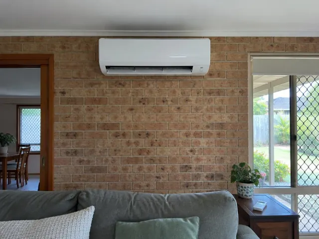 White split system on a brick interior wall above a living room couch in Pacific Pines