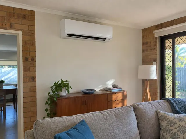 Wall-mounted split system above a sideboard in a brick and plaster living room in Carrara